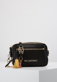 Černá kožená crossbody taška se zlatými detaily, zipovými prvky, embosovaným logem a barevným třásněm v růžové, žluté a červené barvě.