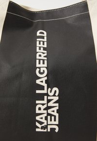 Svart tøyveske med fet hvit tekst "KARL LAGERFELD JEANS." Distinkt tre-tone design med kontrasterende sømdetaljer.