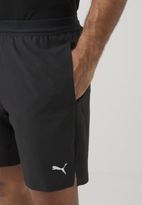 Sorte treningsshorts med lett materiale, elastisk midjebånd, sidelommer og en hvit Puma-logo nær kanten.