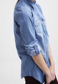 Ljusblå denimskjorta med knapp-down krage, två bröstfickor och uppvikt ärm. Mjuk textur med en avslappnad passform.