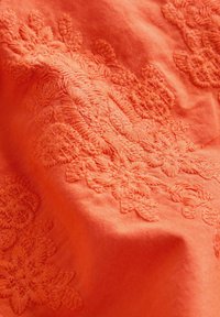 Oranger Stoff mit erhabener Blumenstickerei, der Textur und gestickte Blatt- und Blumenmuster zeigt.