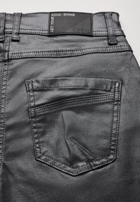 Zadní kapsa a pas černých džín z denimu s černou cedulkou s nápisem "Nech svou duši zářit" a "Cecil."