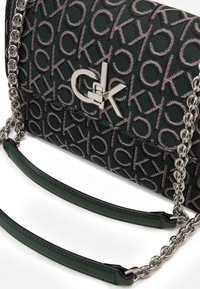 Mørkegrøn crossbody taske med gentaget lyserødt "ck" mønster, sølvfarvet "ck" logo lås, sølvfarvet kædestrop med mørkegrønne læderpuder til skulderen.