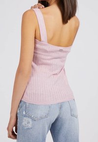 Top in cotone rosa chiaro a costine con spalline larghe e schiena scoperta, abbinato a jeans azzurri chiari strappati con tasche posteriori.