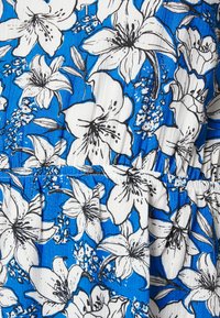 Tecido floral azul com grandes lírios brancos e menores acentos pretos. Apresenta pregas perto da cintura, criando textura e contraste de padrões.