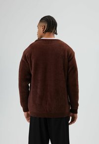 Bruine, pluizige trui met een ronde hals, lange mouwen en geribbelde boorden, van achteren weergegeven. Zachte textuur en een ontspannen pasvorm.