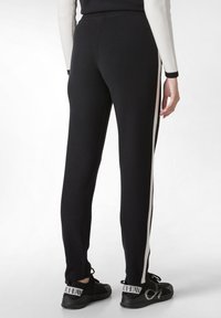 Zwarte gebreide broek met een witte zijstripe, met een aangesloten ontwerp en een elastische tailleband, gecombineerd met zwarte sneakers.