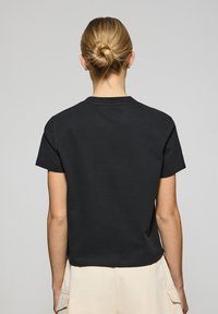 Svart bomullströja med rund halsringning och korta ärmar, med en cropped snitt, slät textur och minimalistisk design.