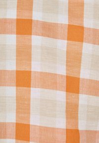 Katoenen stof met een oranje en crèmekleurige geblokte patroon. De textuur is geweven en vertoont verschillende tinten oranje en lichtbeige vierkantjes.