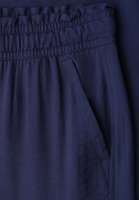 Gros plan sur un pantalon bleu marine avec une taille élastique et une poche latérale, montrant la texture du tissu et les détails des coutures.