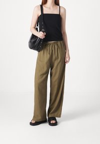 Zwarte mouwloze top, losse olijfgroene broek met trekkoord in de taille, en zwarte sandalen. Zwarte schoudertas met zilverkleurige accenten.