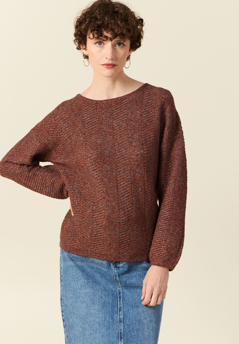 Brauner, strukturierter Strickpullover mit weitem Ausschnitt und Ballonärmeln, kombiniert mit einem Jeansrock. Beide Kleidungsstücke haben lässige Designs.