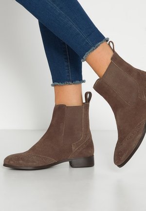 Bruine suède enkellaarsjes met elastische zijpanelen en lusjes, gedragen met donkerblauwe skinny jeans met rafelige zoom.