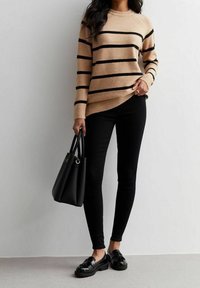 Beige randig tröja med svarta horisontella ränder, ihop med svarta tajta jeans och glansiga svarta loafers. Svart handväska hålls i handen.