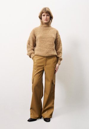 Beige textuur turtleneck trui gecombineerd met losse, camel-kleurige cargobroek met zijzakken en zwarte schoenen.