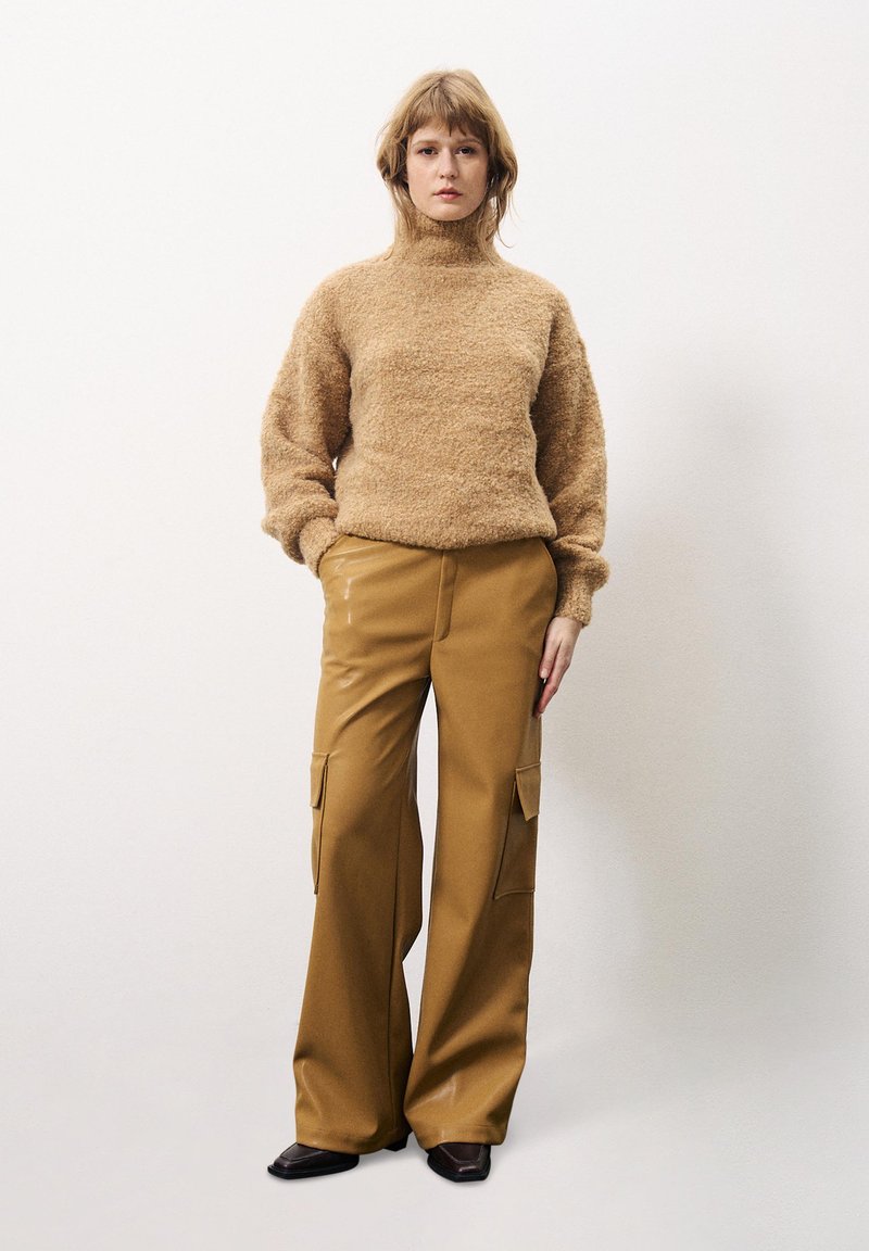 Beige textuur turtleneck trui gecombineerd met losse, camel-kleurige cargobroek met zijzakken en zwarte schoenen.