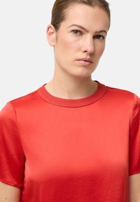 Rød kortærmet skjorte lavet af glat, let stof. Har en rund, ribbet halsudskæring og enkelt design uden pynt.