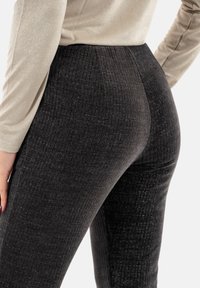 Leggings negros de talle alto, texturizados con un patrón de canalé y un sutil brillo, combinados con un top metálico claro y ajustado.