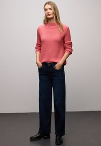 Pull en tricot côtelé rose avec un col montant, associé à un jean pattes d'éléphant bleu foncé et des bottines noires. Tenue simple et décontractée.