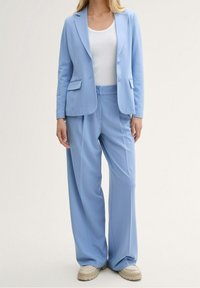 Lichtblauw op maat gemaakt kostuum met een blazer met notch-revers en twee zakken, gecombineerd met brede broekspijpen. Glad textiel.
