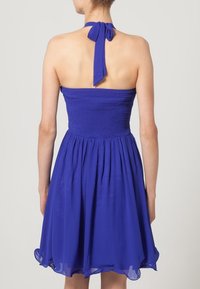 Kort blå klänning med en åtsittande smockad bodice och utsvängd kjol. Har en halterneckband och genomskinligt tyg för en lätt känsla.