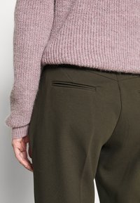 Lichtroze gebreid sweater met een textuurafwerking, gecombineerd met donker olijfgroene op maat gemaakte broek met achterzakken en een gladde stof.