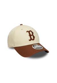 Gorra de béisbol con una parte superior color crema y visera marrón. Presenta una "B" bordada en marrón oscuro y una pegatina de logo en el borde.