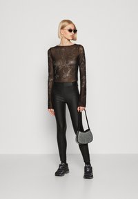 Fekete áttetsző, hosszú ujjú felső ezüst színű virágmintával, fényes fekete leggings-szel és csillogó kézitáskával párosítva. Fekete sportcipő.