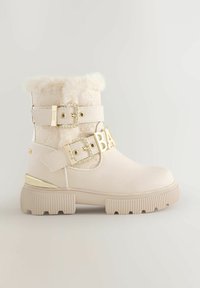 Stivale alla caviglia in ecopelliccia beige, con doppie cinghie dotate di fibbie dorate e un dettaglio decorativo "BA" sul lato.