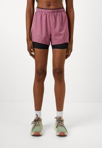 Lightweight, purple athletic shorts with an elastic waistband, layered over black fitted shorts. Worn with green and beige running shoes.