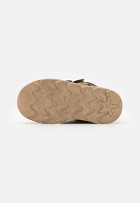 Chaussure marron avec une semelle en caoutchouc texturée présentant un motif en vagues, agrémentée d'un logo étoile au talon. Conception flexible et légère.