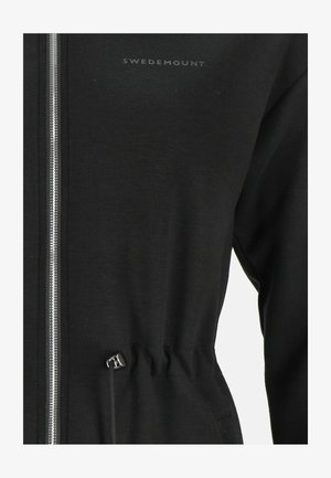 Black zip-up jacket with a soft texture, featuring a cinched waist and silver hardware. Logo printed in gray on the upper left side.