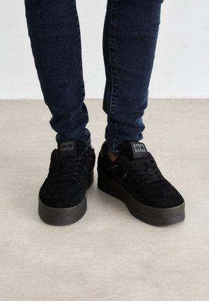 Baskets en daim noir avec une épaisse semelle en caoutchouc, dotées de lacets noirs et d'un design de bout rond et plat. Agrémentées d'un patch logo sur la languette.