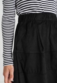 Mustapintainen mokkahame, jossa on kerrostettu muotoilu ja joustava vyötärö. Yhdistettyinä laivastonsiniseen ja valkoiseen raitapaitaan, jossa on pitkät hihat.