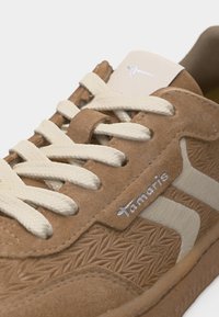 Light brown suede sneaker with textured patterns, white fabric lace-up, and white "Tamaris" logo on the side.