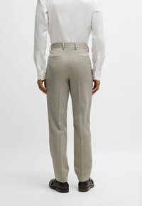 Pantaloni grigi chiaro, su misura, con un sottile motivo a righe, dotati di tasche laterali e posteriori, abbinati a una camicia bianca a maniche lunghe.