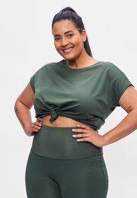 Green activewear set featuring a loose, short-sleeved top with a knotted front and high-waisted leggings, both in a smooth, stretchy fabric.
