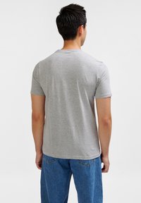 Camiseta gris de manga corta hecha de una mezcla de algodón, con un cuello redondo y una textura suave, combinada con jeans de mezclilla azules.