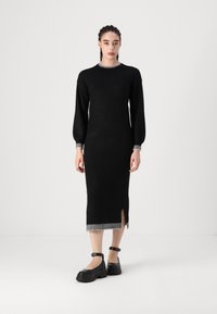 Crna, uska pletena haljina s dugim rukavima, okruglim izrezom i bočnim prorezom; ima prugasti naglasak na izrezu i rubu.