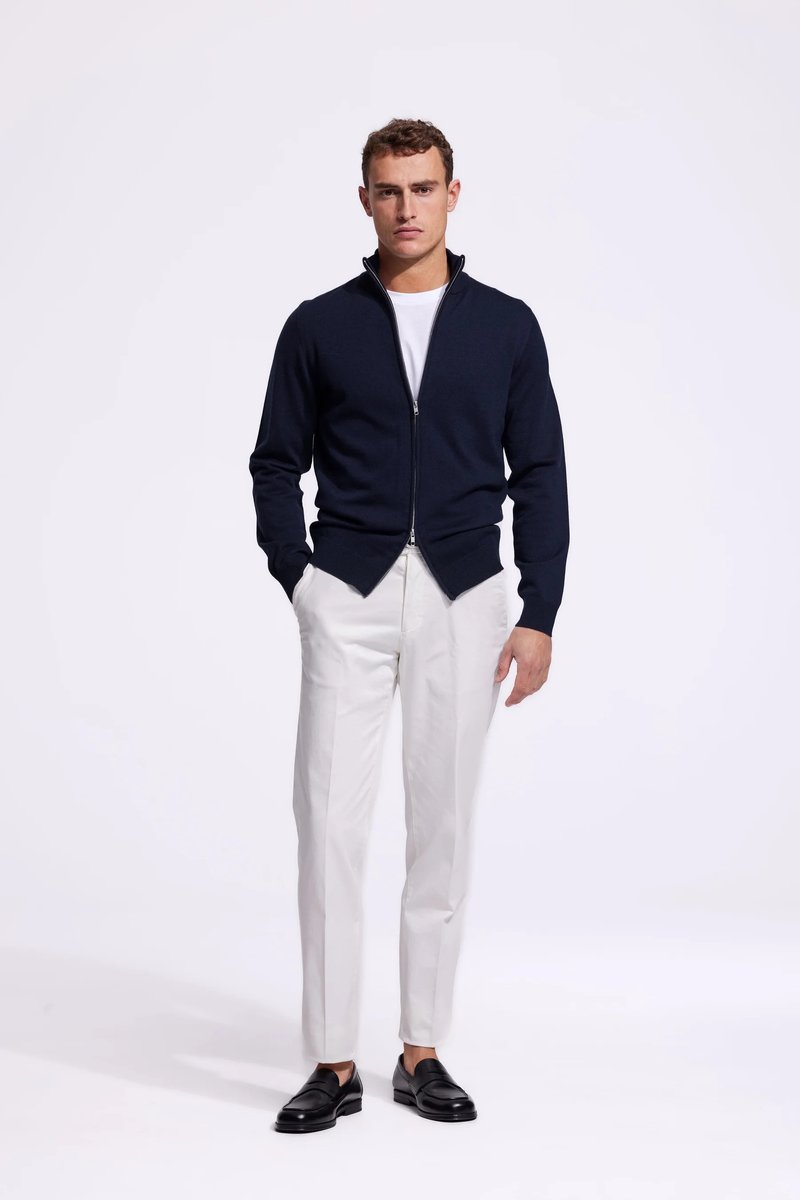 Marineblauwe zip-up trui met opstaande kraag, gedragen over een wit overhemd. Gecombineerd met op maat gemaakte witte broek en zwarte instappers. Gladde textuur.
