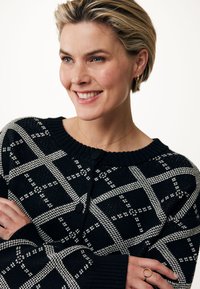Svart och vit rutmönstrad stickad tröja med rund halsringning och knappstängning, med ribbade ärmslut och strukturerad tyg.
