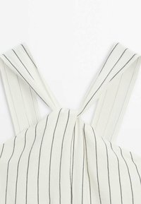 Tissu blanc avec de fines rayures noires verticales noué en haut, formant deux larges bretelles.