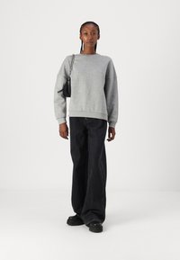 Gray cotton sweatshirt with dropped shoulders, paired with loose-fitting dark jeans. Model holds a small black handbag with a chain strap.