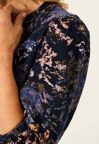 Marineblaues Gewebe mit einem mehrfarbigen abstrakten Muster in Pink, Gold und Blau. Verfügt über geraffte Ärmel und eine weiche Textur.