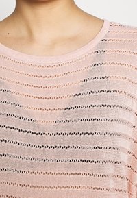 Maglione rosa chiaro con scollatura rotonda, caratterizzato da strisce orizzontali di lavorazione a giorno e sezioni solide per un contrasto di texture.