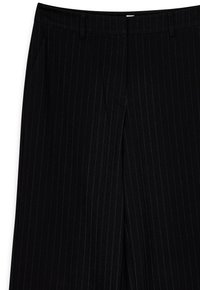 Zwarte pinstreepbroek met een tailored fit, voorzien van zijzakken en een vlakke voorkant. Gemaakt van een gladde stof met een lichte glans.