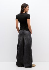 Black fitted t-shirt with short sleeves, paired with loose, high-waisted dark gray jeans featuring back pockets and a smooth texture.