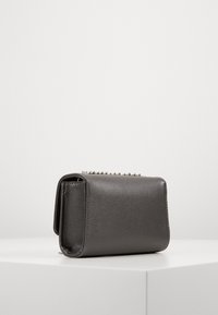 Piccola borsa a mano in pelle testurizzata grigio scuro con tracolla in catena argentata, vista di lato su una superficie bianca contro uno sfondo neutro.