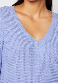 Jasnofioletowy dzianinowy sweter z dekoltem w serek, teksturowaną tkaniną i prążkowanymi wykończeniami przy dekolcie oraz rękawach.