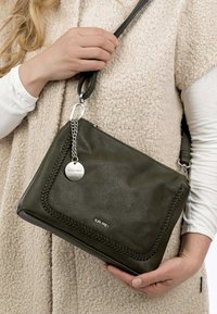 Borsa a tracolla in pelle verde oliva con texture intrecciata, hardware in argento e un'etichetta metallica. Design compatto con tracolla regolabile.